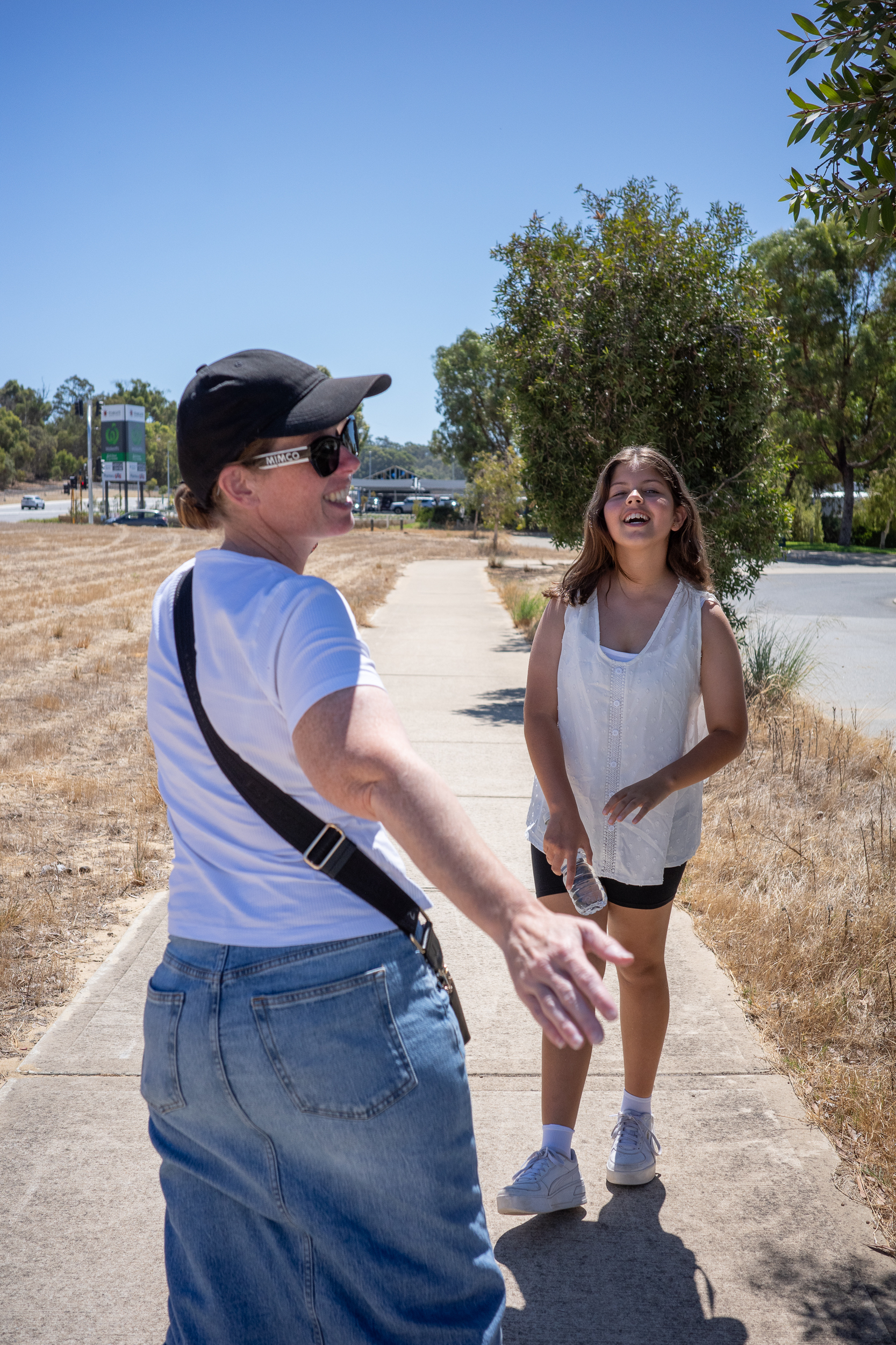 A woman and a girl are walking on a sidewalk, with the woman looking back towards the camera and the girl smiling.